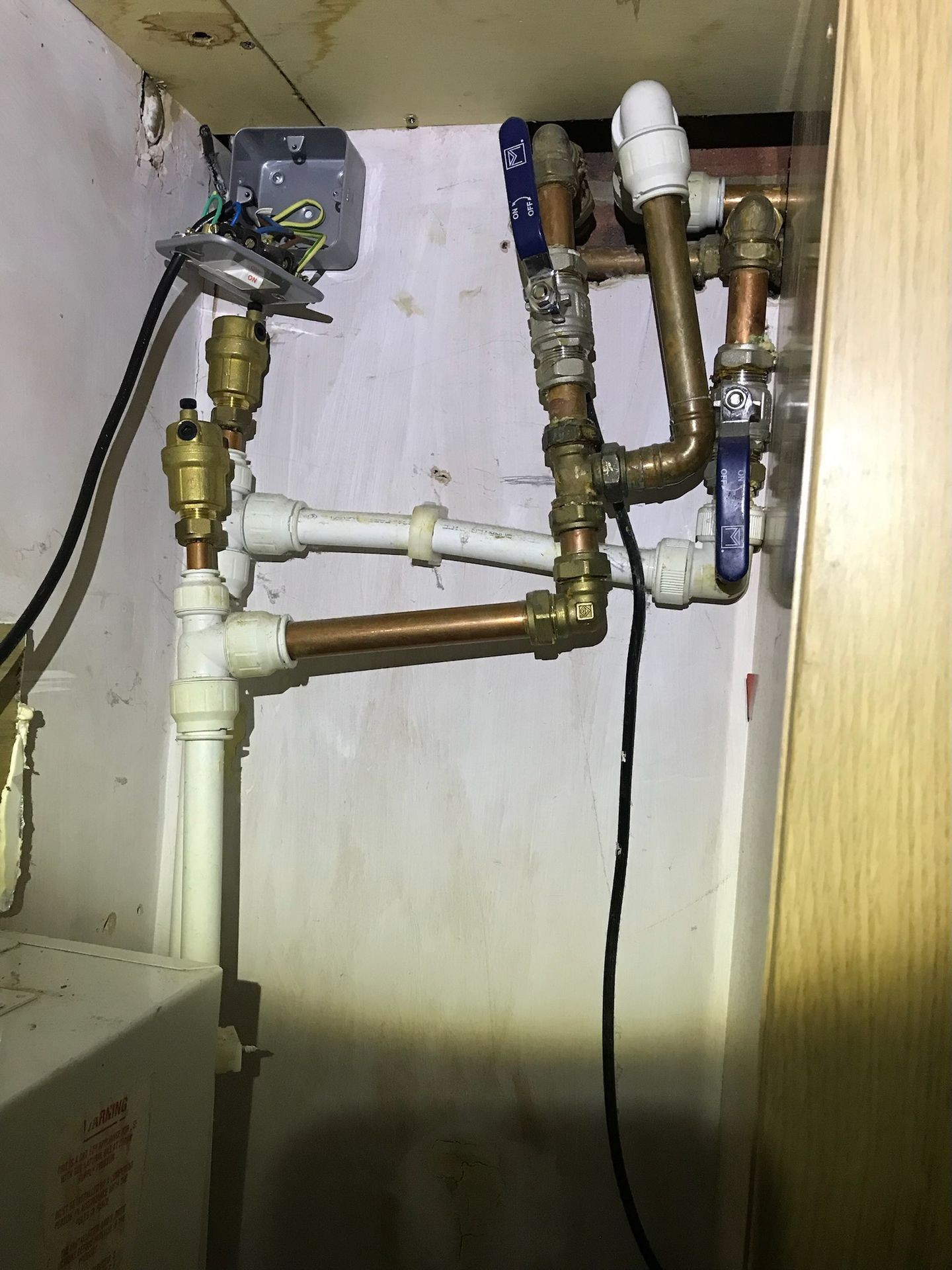 Plumbing setup with various copper and plastic pipes and valves in a dimly lit space.